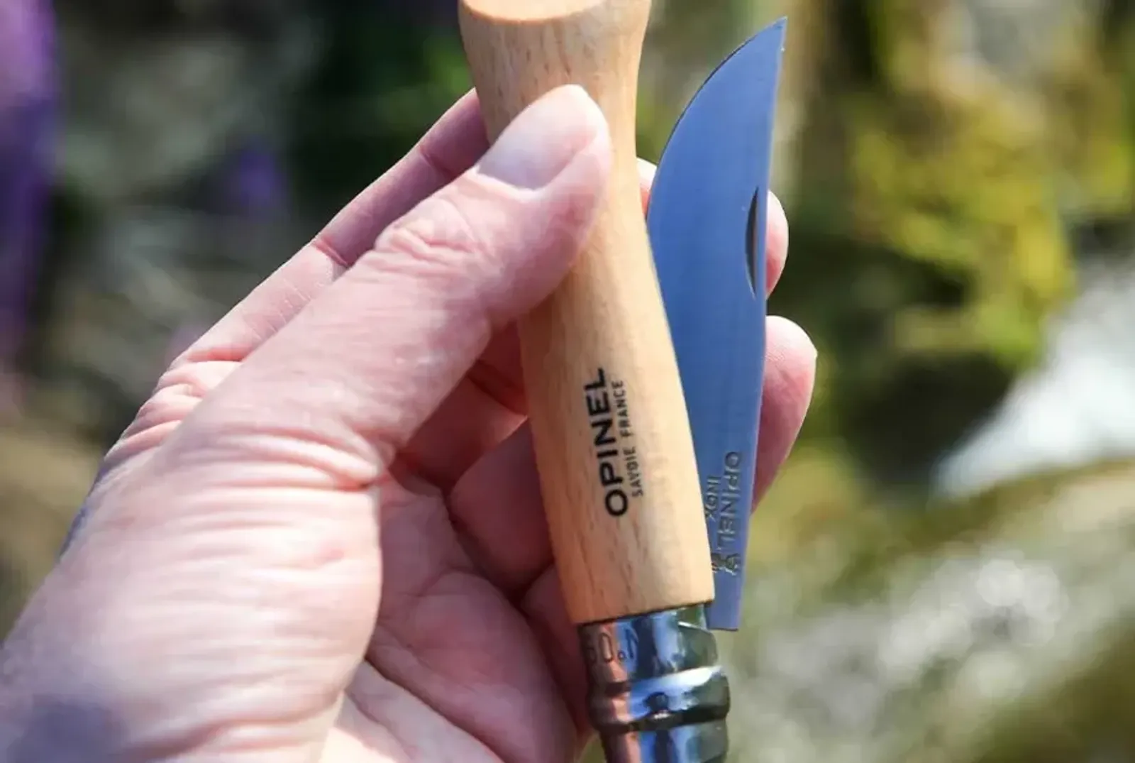 Opinel N09 kniv med trähandtag och rostfritt stål blad hållen utomhus med naturlig bakgrund