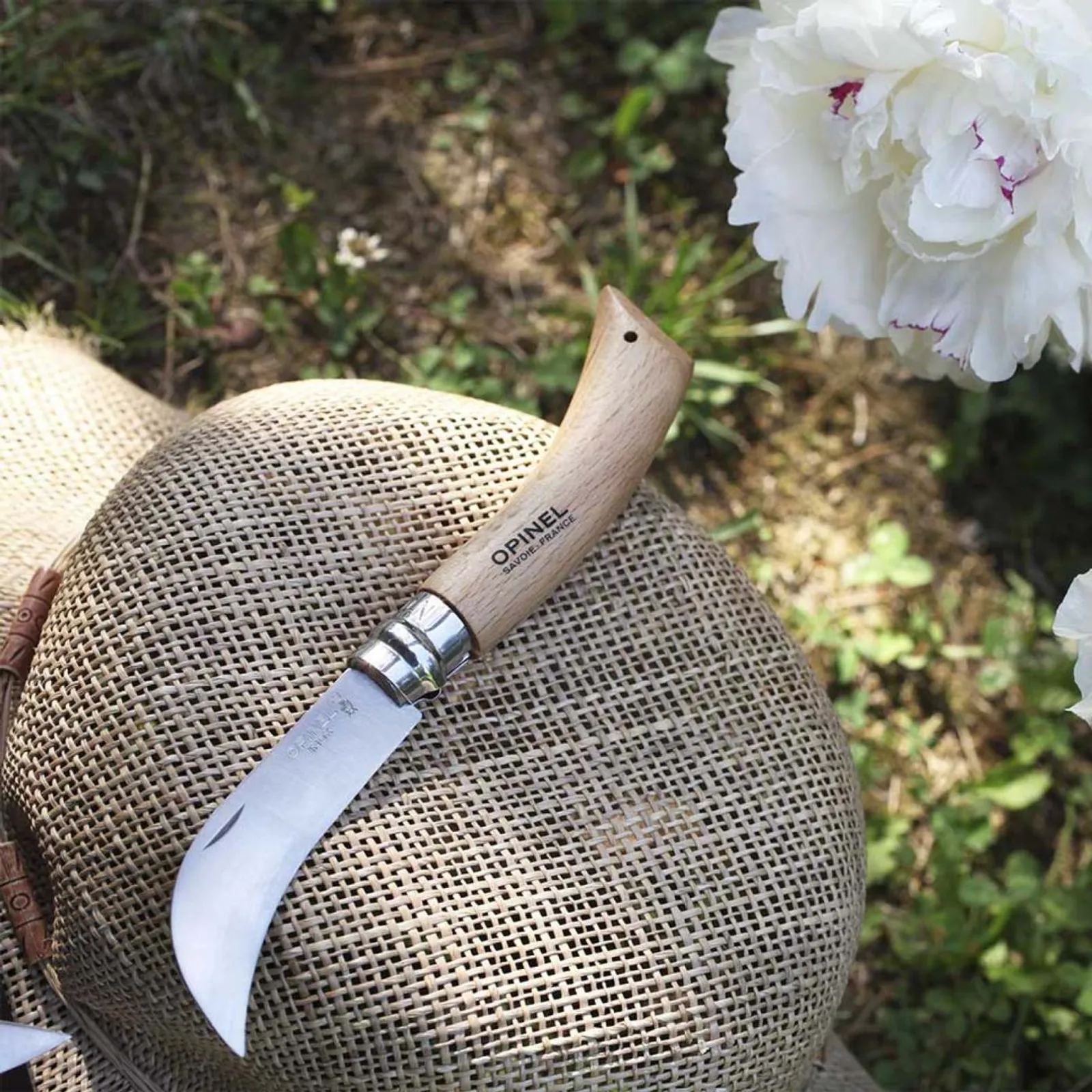 Opinel N08 beskärningskniv med trähandtag och rostfritt stål blad vilar på säckväv med blommor i bakgrunden