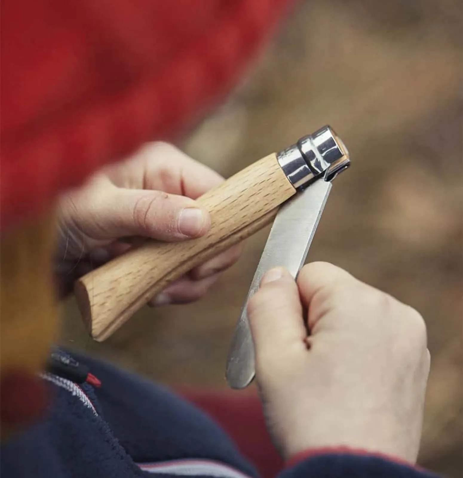 Opinel fällkniv med trähandtag klipper kvist i naturlig utomhusmiljö - rostfritt stål blad synligt