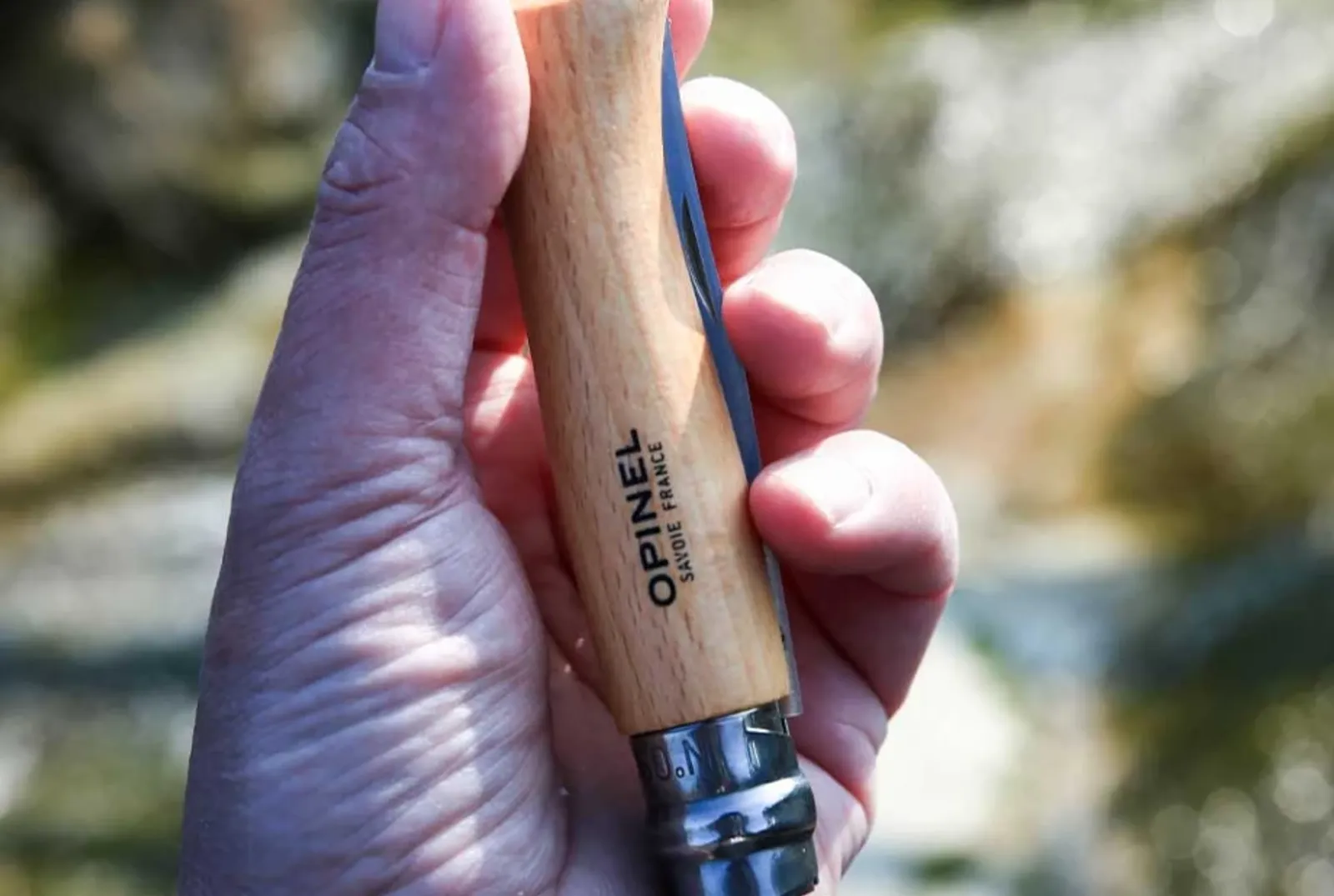 Opinel N09 kniv hållen i hand med trähandtag och rostfritt stål blad mot naturlig utomhusbakgrund